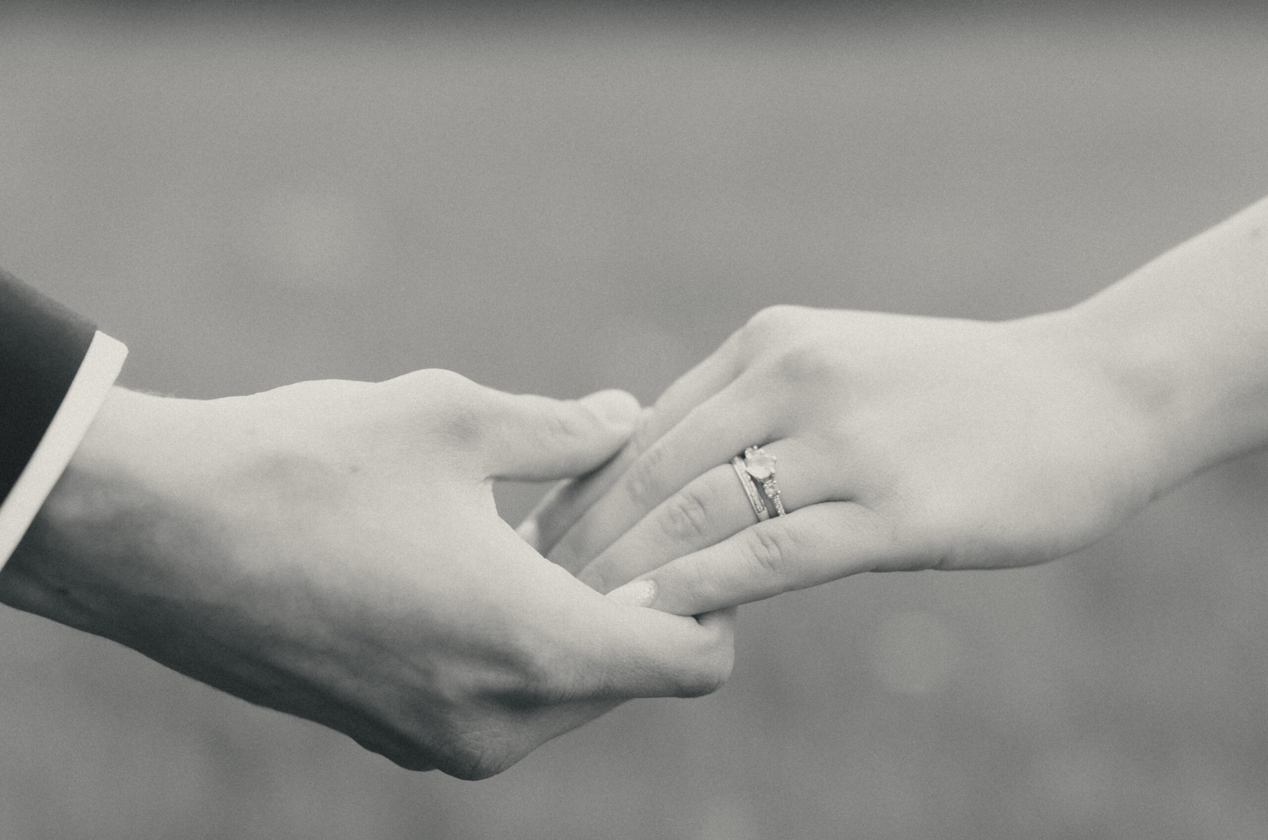 A close-up photo on a bride and her groom holding hands with their wedding rings visible.